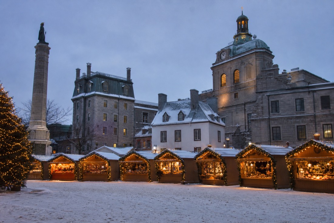 Christmas market stalls glowing at dusk on a snowy square in Old Quebec City