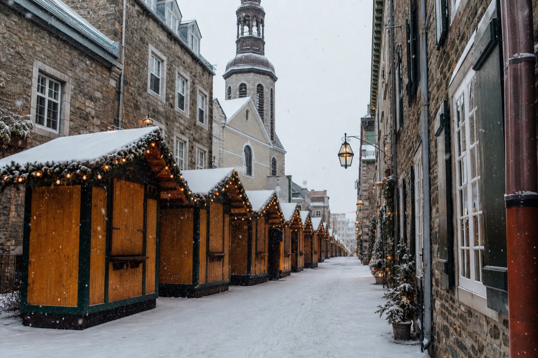 Wooden Christmas market stalls with lights along rue Sainte-Anne in Old Quebec under falling snow