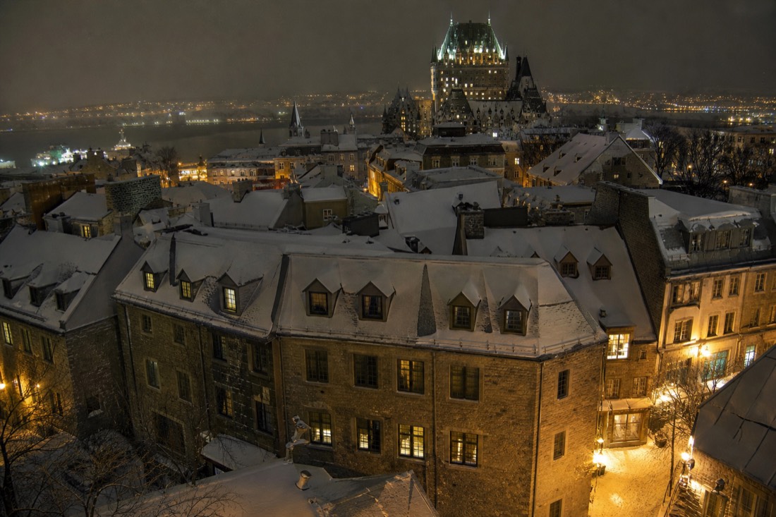Snow-covered Old Quebec rooftops at night in December with warm light from windows and street lamps