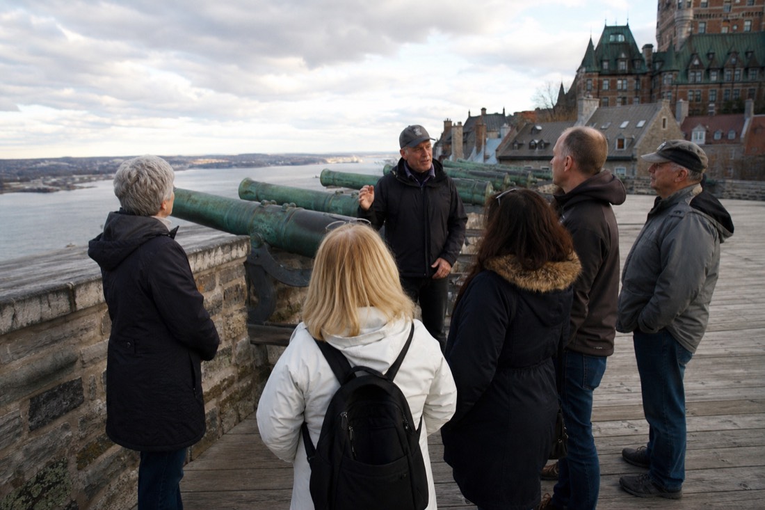 Small tour group listening to a guide on the ramparts of Old Quebec near a row of historic cannons