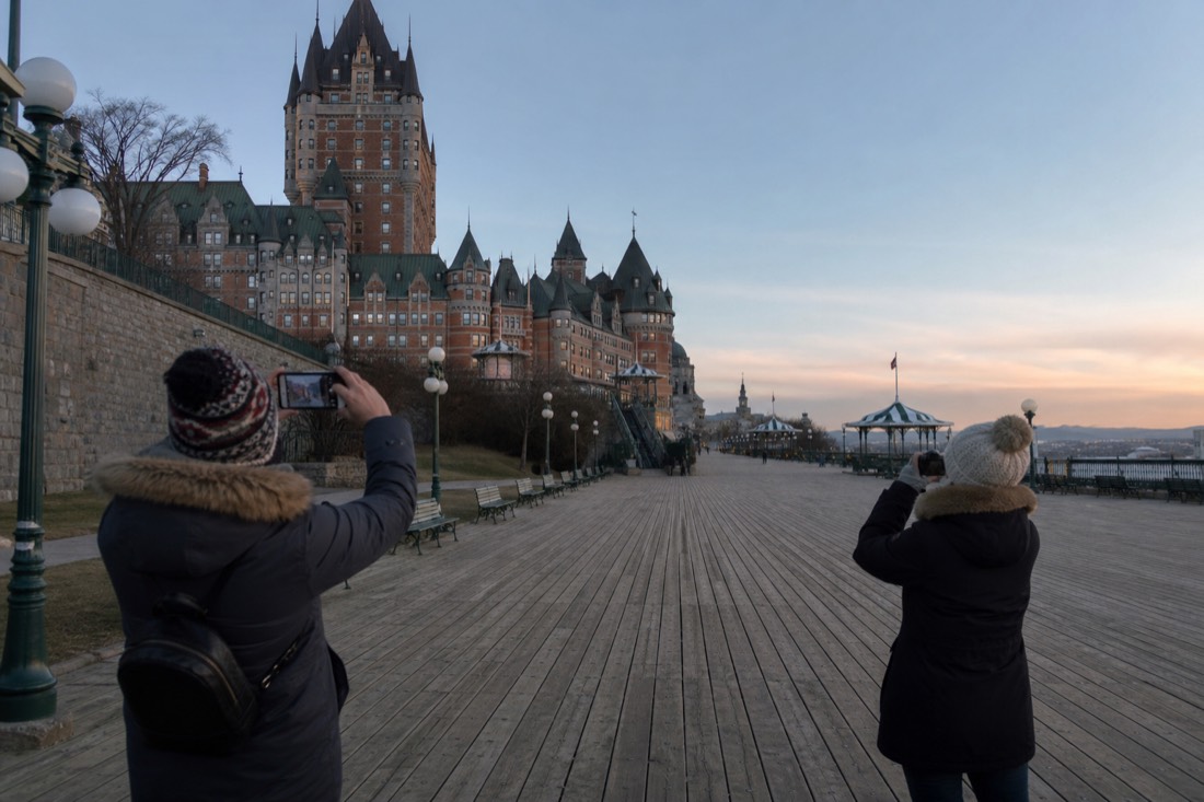 Tourists photographing the Château Frontenac from the boardwalk at dusk