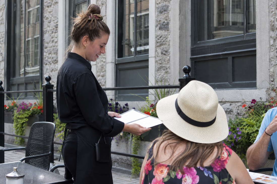Server presenting an English menu to visitors at a restaurant terrace on Rue Saint-Jean in Old Quebec
