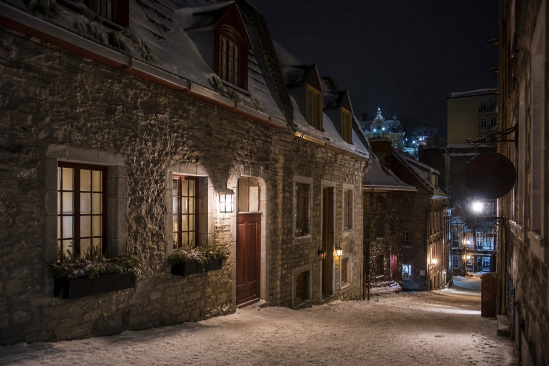 A snow-covered lane in Old Quebec at night with warm light spilling from shop windows