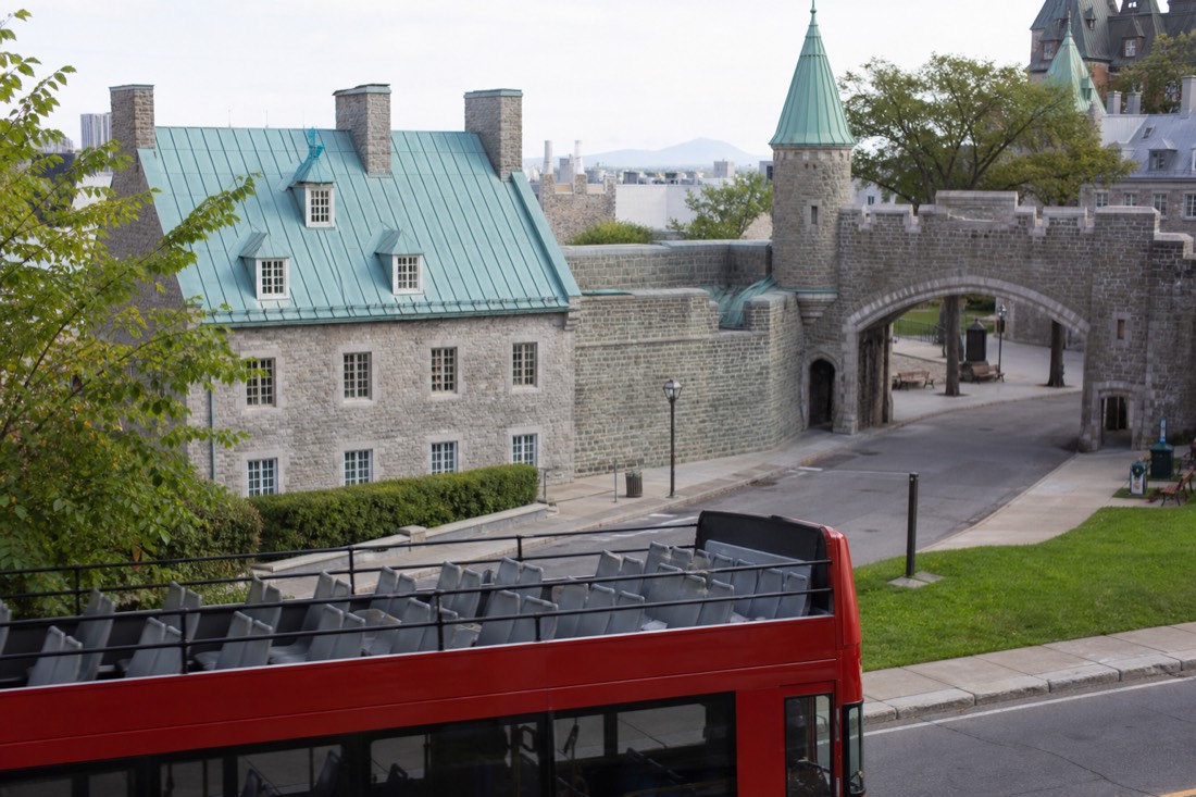 Open-top double-decker sightseeing bus passing stone buildings near the walls of Old Quebec