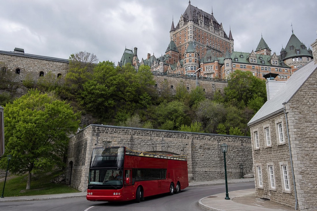 Open-top double-decker sightseeing bus rounding a corner below the old stone fortifications of Quebec City