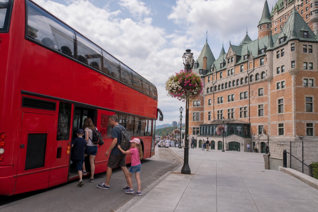 Family with two children boarding a double-decker tour bus at a stop in Quebec City in summer