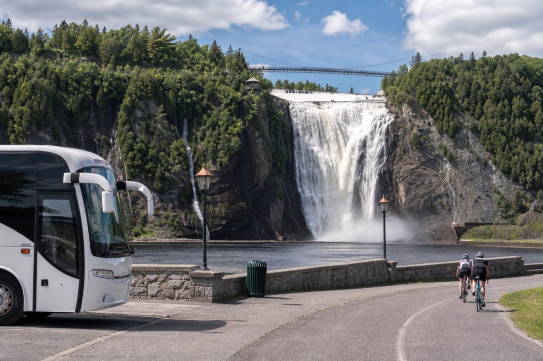 Tour coach parked at Montmorency Falls with cyclists arriving on the riverside path from Quebec City
