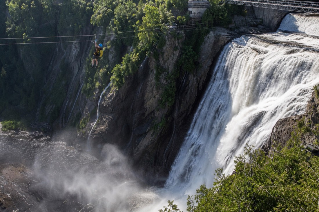 Zipline rider crossing the 300-metre line in front of Montmorency Falls with the basin far below