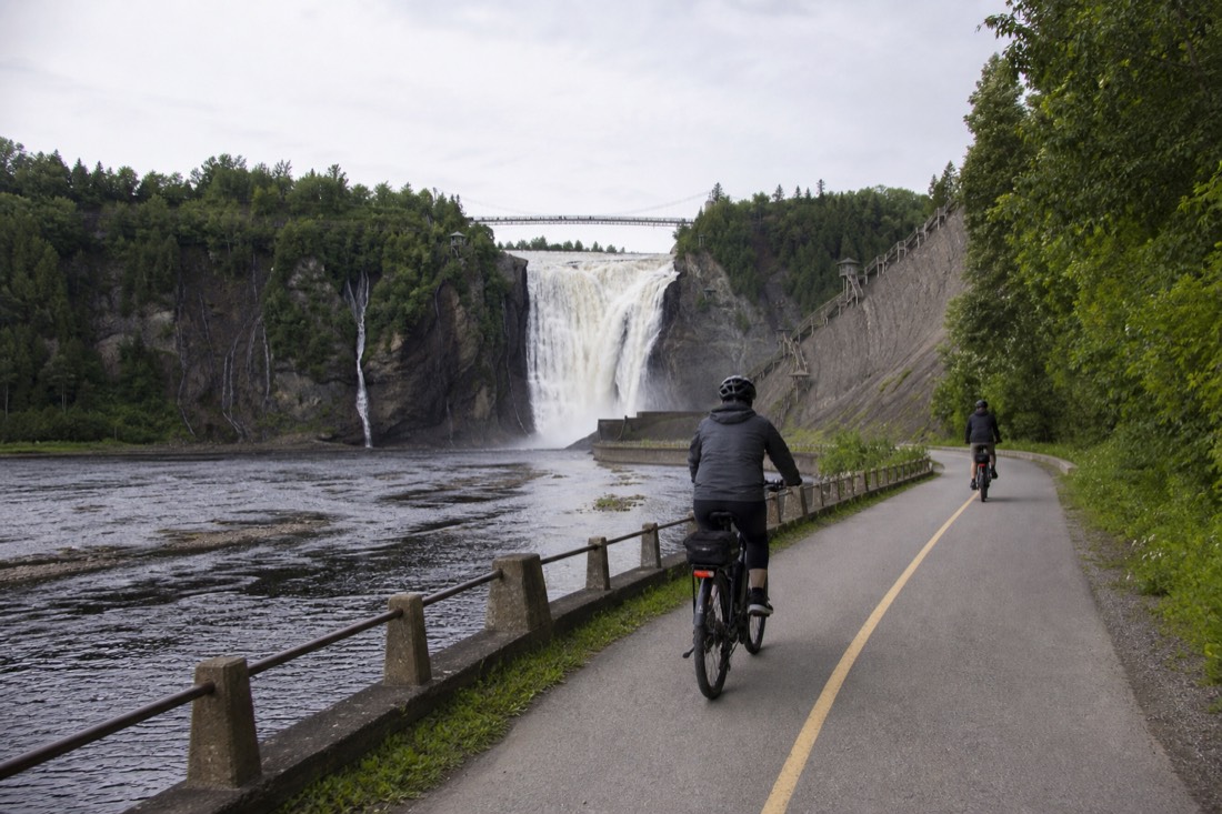 Cyclists on e-bikes riding the riverside path toward Montmorency Falls near Quebec City